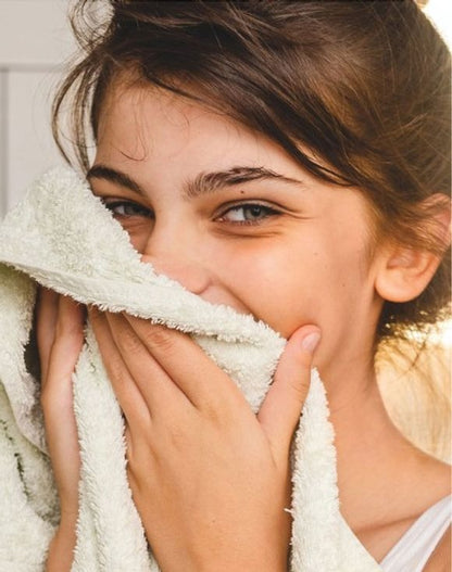 Smiling girl holding a soft towel to her face, showcasing clean, fresh skin and joy after using Skin So Soft Soft & Sensual Bar Soap.